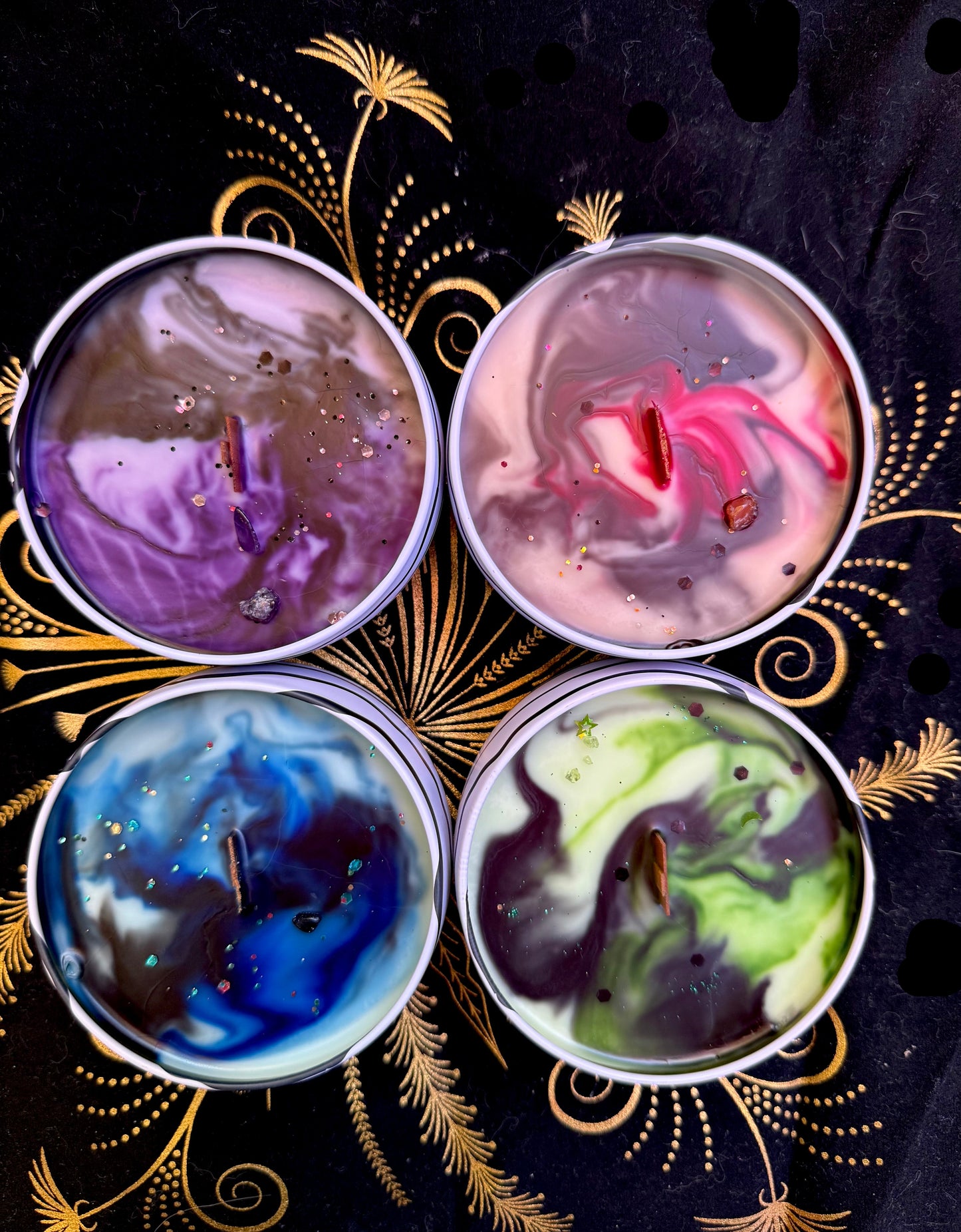 Four colorful candles in tins on a decorative black background with gold accents.