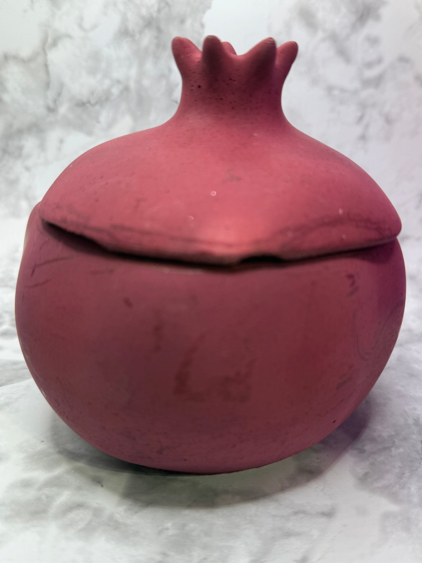Pomegranate shaped candle vessel against a white marble background 