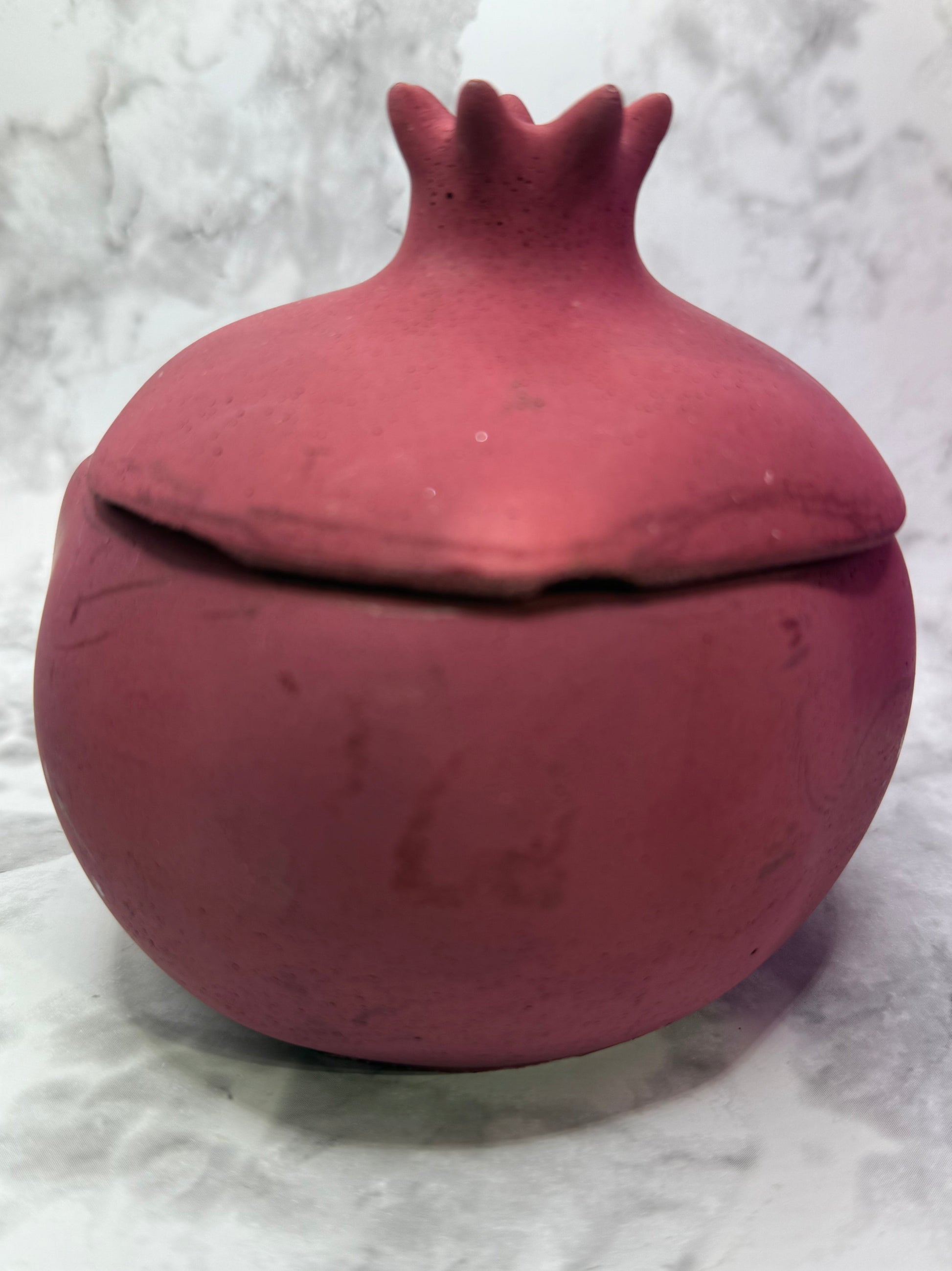 Pomegranate shaped candle vessel against a white marble background 